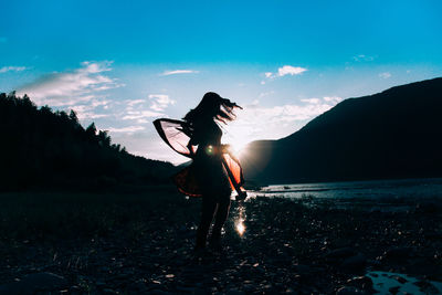 Woman holding scarf on field against blue sky during sunset