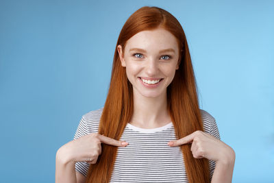 Woman pointing self against blue background