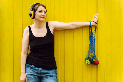 Portrait of young woman standing against yellow wall