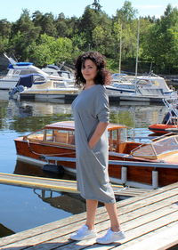 Smiling young woman standing on pier by moored boats over lake