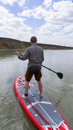 Rear view of man on paddleboard in lake against sky