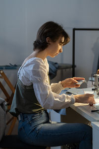 Young female seamstress sew on sewing machine, tailor sit at workplace in fashion workshop atelier
