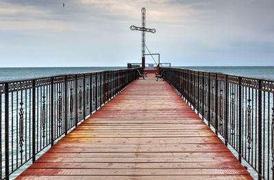 Cross on pier by sea against sky
