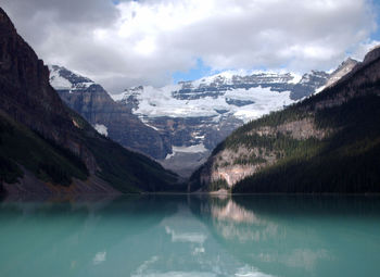 Blue lake louise in front of mountains against cloudy sky