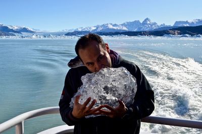 Portrait of man eating ice while standing on boat in sea during winter