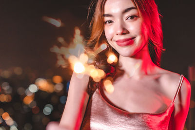 Portrait of smiling young woman holding illuminated outdoors