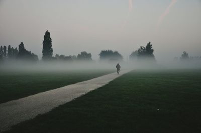 Person riding bicycle on footpath against sky during foggy weather