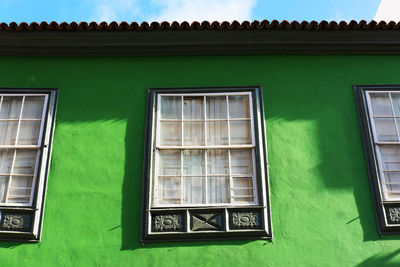 Low angle view of windows on green wall of building