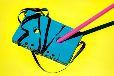 High angle of blue retro cassette with messy magnetic tape and pencil for rewind placed on yellow background in studio