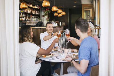 Happy friends raising toast while sitting in restaurant