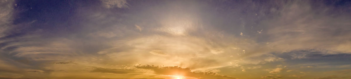 Low angle view of sunlight streaming through clouds during sunset