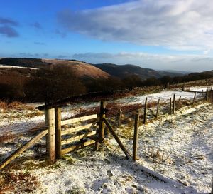 Fence on snow covered landscape against sky