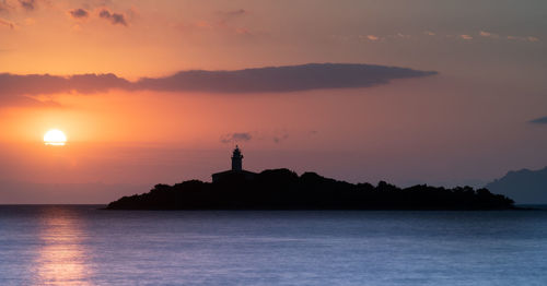 Silhouette lighthouse by sea against sky during sunset