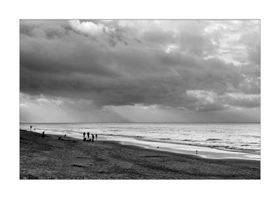People at beach against cloudy sky