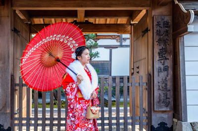 Woman wearing traditional clothes while standing with red umbrella