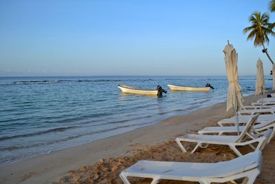 Deck chairs at beach against blue sky during sunset