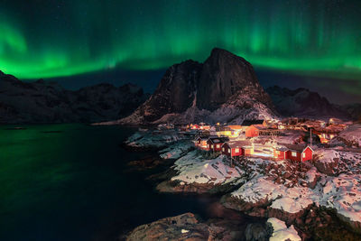 Illuminated buildings by mountain against sky at night during winter