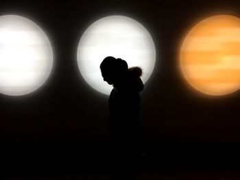 Silhouette boy standing against illuminated lights at night