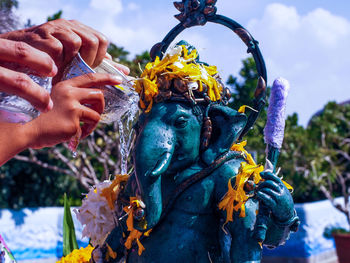 Cropped hands pouring water on ganesha statue against sky