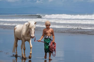 Full length of shirtless boy walking on beach against sky