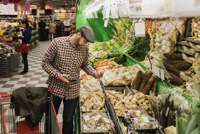 Man holding smart phone while buying root vegetable in supermarket