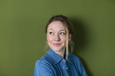 Thoughtful young woman wearing denim shirt in front of green wall