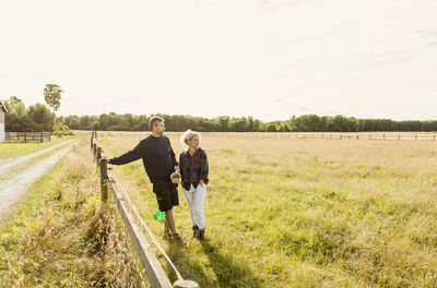 Couple looking away while standing on grassy field against clear sky