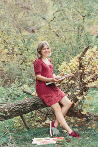 Portrait of smiling woman sitting on tree trunk in forest
