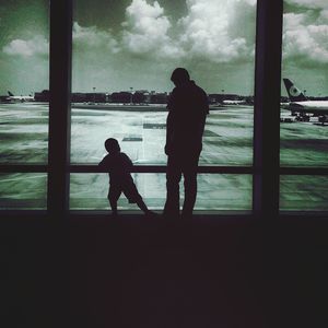 Silhouette father and son standing by railing against sea