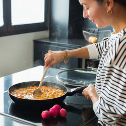 Close up of woman hands adding ingredients while cooking vegetable stew at the modern kitchen