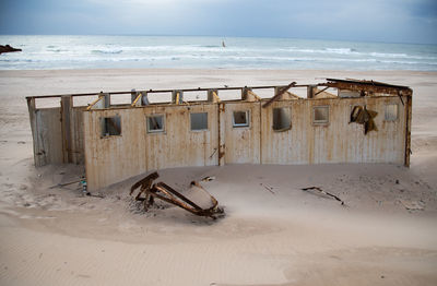 Abandoned lifeguard hut on beach against sky