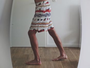 Low section of man standing on wooden floor at home