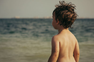 Midsection of shirtless boy at beach