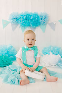 A one-year-old boy in a summer suit with a butterfly sits on the photo zone of his birthday 