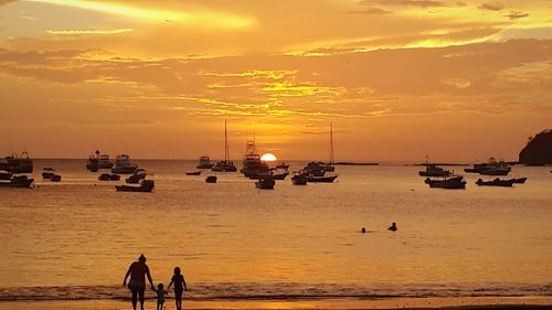 Silhouette people on beach against sky during sunset