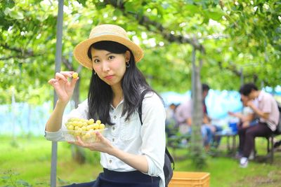 Young woman eating grapes against plants on field