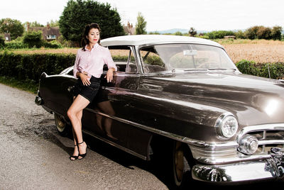 Young woman sitting on car against sky