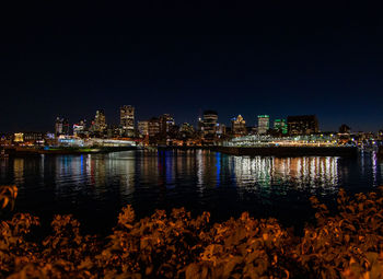 Illuminated buildings by river against clear sky at night