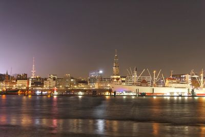 Illuminated city by sea against sky at night