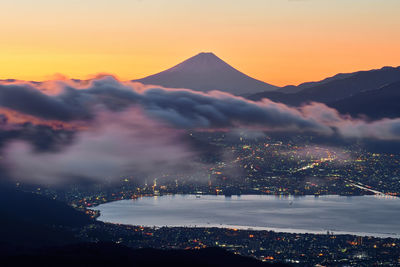 High angle view of illuminated cityscape by lake against orange sky 