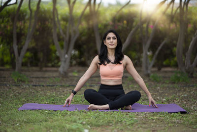 Full length of woman meditating while sitting outdoors