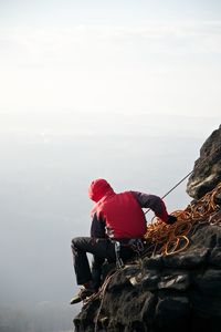 Side view of person sitting on rock formation during foggy weather