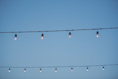 Low angle view of illuminated light bulbs hanging against clear sky