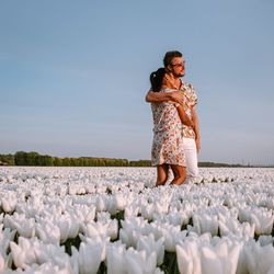 Couple embracing amidst white flowers against sky