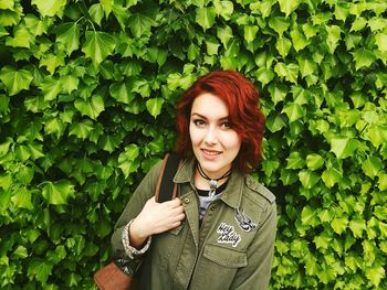 Portrait of redhead woman standing against green creeper plants