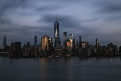 Illuminated buildings in city against cloudy sky