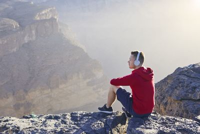 Side view of young man sitting on rocky mountain