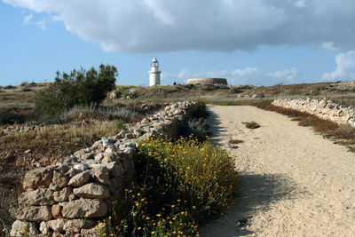 Lighthouse on field by building against sky