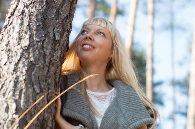 Portrait of smiling young woman against tree trunk