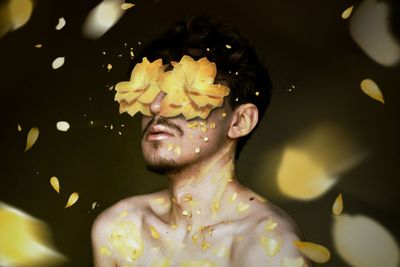 Shirtless young man with petals against black background
